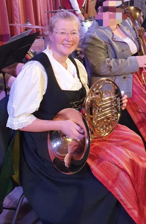 Die Musiklehrerin in bayerischer Tracht lächelt in die Kamera und hält ein Horn.