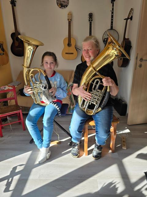 Die Musiklehrerin und eine Schülerin halten gemeinsam lächelnd ihre Tenorhörner.